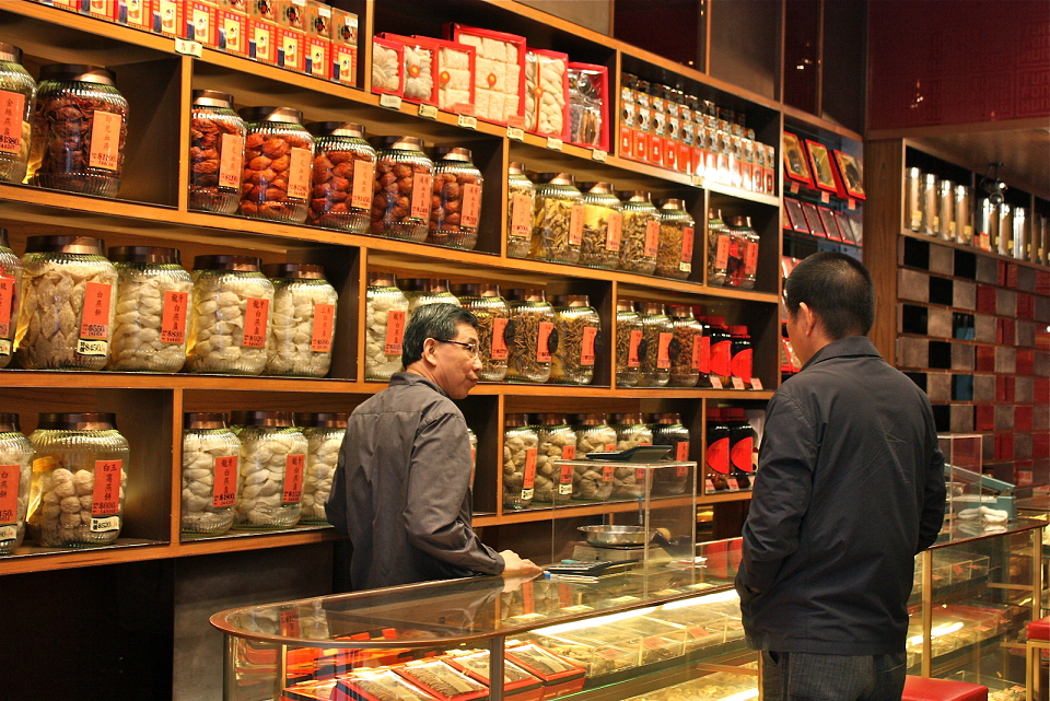 An herb seller and potential buyer stand in a well stocked Chinese herb shop.