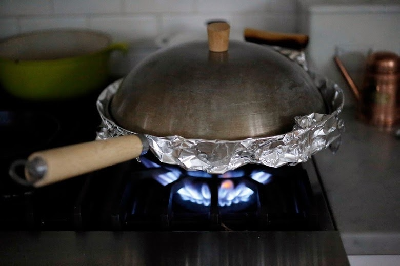 sugar smoking wok wrapped in foil paper and covered with lid on a burner fire.
